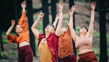 Photo of four dancers wearing red and orange clothes with their hands raised in the air