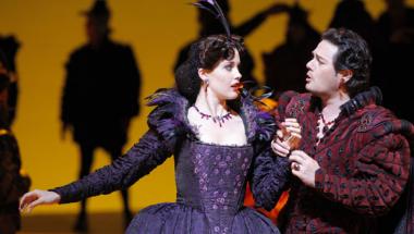 A photograph of Pene Pati as the Duke of Mantua and Zanda Svede as Maddalena in Verdi's "Rigoletto." The two stand close, gazing at one another as the Duke of Mantua clutches Maddalena's hand. Photo by Cory Weaver/San Francisco Opera