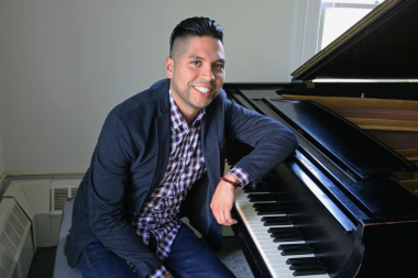 Musician Erick Peralta smiles and leans over the keyboard of a grand piano