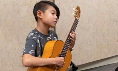 A Colburn Community School Suzuki guitar student holding a guitar.