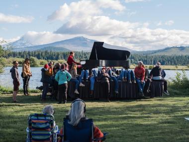 Hunter Noack plays the piano on a stage and audience members surround him and the piano listening to him play