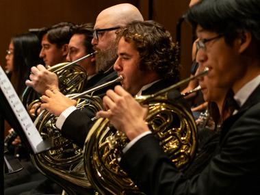 A closeup of four brass French horn players of the UC Davis Symphony Orchestra in concert black attire.