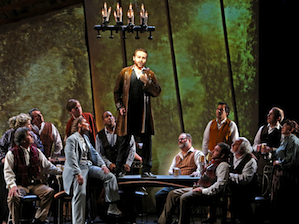 Betany Coffland as Nicklausse (in light suit), Mathew Pierce as Hermann (taller, blond, in red outfit), Darron Flagg as Nathanaël (in black vest) and Christopher Bengochea as Hoffmann (standing on the table)